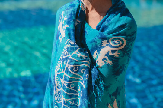 Woman wrapped in a blue patterned blanket standing by a swimming pool