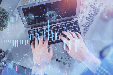 Double exposure of man's hands typing over laptop keyboard and forex chart hologram drawing. Top view. Financial markets concept.