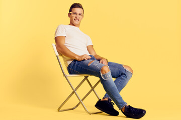 Cute man sitting on a chair white t-shirt jeans lifestyle modern style yellow background