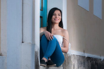 Latin girl sitting on a blue wooden doorway with a side view