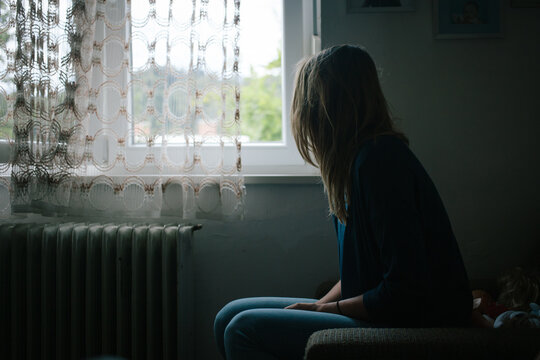 Young woman sitting and staring outside through the window.