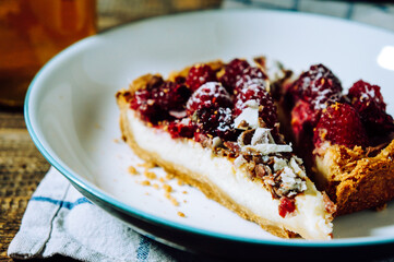 cheesecake with raspberries and chocolate in a white plate on a wooden table, copy space