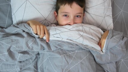 Portrait of a scared boy in bed getting out from under the cover and covering his face with blanket, children kid fears concept
