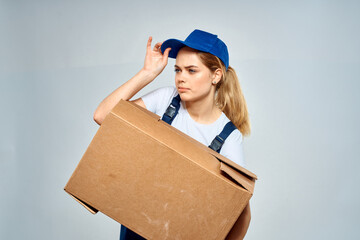 A woman in a working uniform with a box in the hands of a delivery service delivery service light background