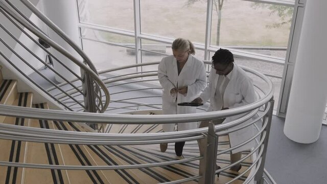 Doctors In Hospital On Staircase Discussing Analysis Of New Corona Virus Using Digital Tablet