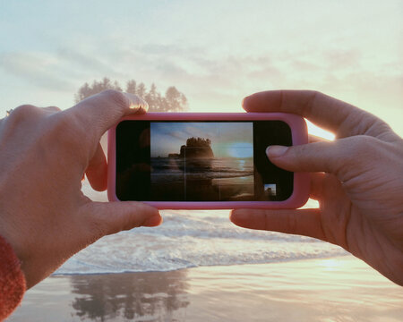 hands holding a phone, taking a picture of a sunset