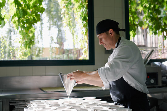 Cook pouring fruit juice with a piston funnel in dessert plates