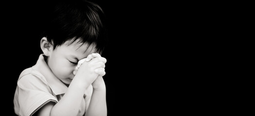 Little toddler boy keep praying for world pandemic coronavirus Covid-19 black banner background.Stay at home praying to GOD.Online church worship in sunday.Hands praying at home.Religion, Christian.