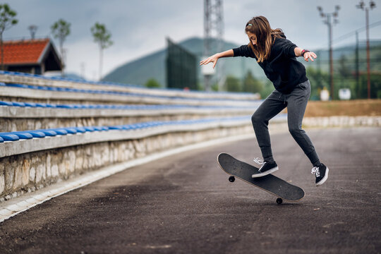Teenage girl performing skateboard tricks on the sports field.