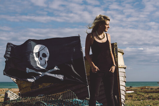 A young woman, pirate flag, and abandoned boat on a beach.