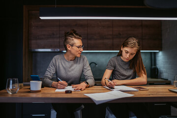 Mother helping her daughter with homework in the kitchen at home - obrazy, fototapety, plakaty