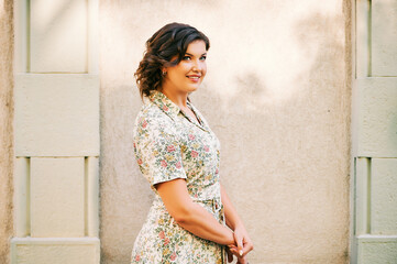 Outdoor portrait of young pretty woman posing next to wall, wearing dress