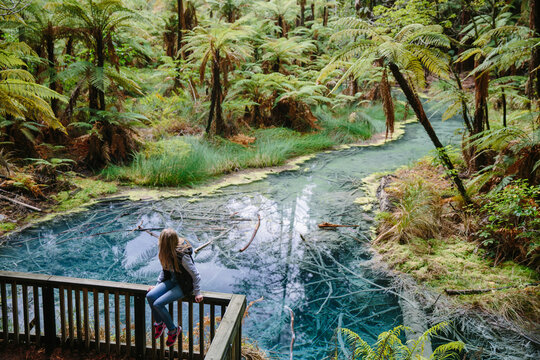 Woman sitting on a fence near clear thermal stream in Whakarewarewa Redwoods Forest