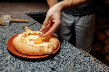 Baker hands preparing khachapuri on kitchen table. cook making traditional georgian treat with raw dough and egg. recipe concept