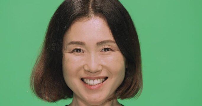Studio, slow motion, a portrait of a laughing Japanese woman against a green screen, London, UK
