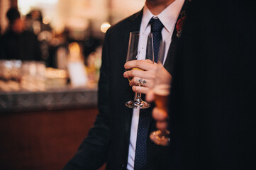Groom with anchor tattoo on ring finger drinking and socializing at wedding party