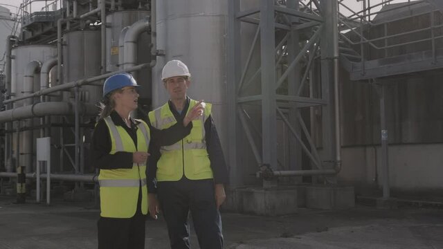 Industrial workers inspecting industrial plant wearing protective workwear and pointing