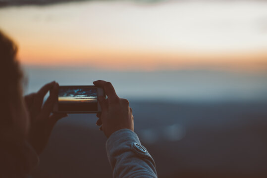 Woman traveling through the mountains taking pictures of the sunset with the mobile.