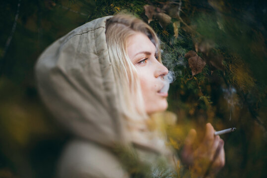 Young blonde woman with a hood on blowing smoke out her mouth