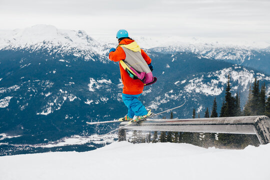 Skier sliding on a rail in a snowpark with mountains in the background in a ski resort