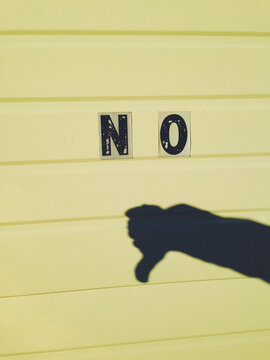 The word NO and shadow of thumb pointing down on yellow garage door