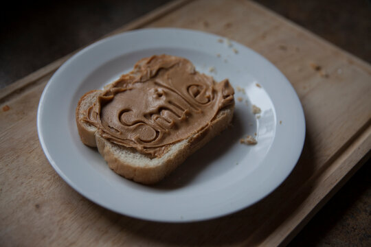 single slice of bread on wooden board with the word smile written into peanut butter