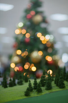 Little pine trees in front of a big Christmas tree in colourful bokeh light