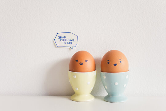 Eggs couple with hand drawn face on the ceramic cup saying "" GOOD MORNING BABE ""