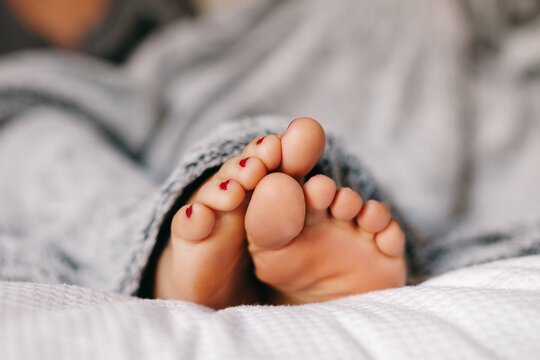Closeup of the foots of a young woman under a blanket at home.