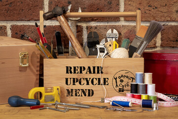 tool box with repair, upcycle, mend stencil text surrounded by repair tools on bench, consumer...
