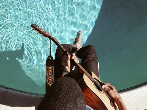 Guy playing guitar on diving board over pool