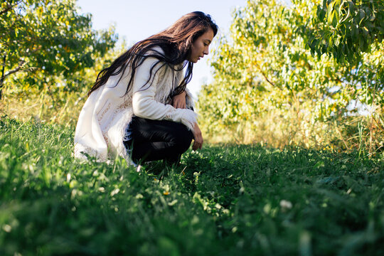 beautiful girl crouches in an apple orchard examines the ground