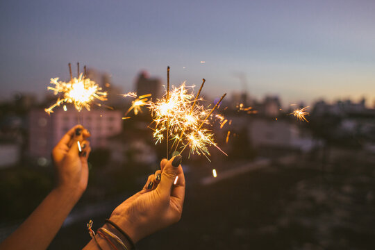 Woman's hands holding sparkle light sticks during sunset in the city on a rooftop