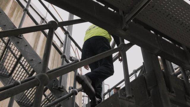 Industrial Worker Walking Up Stairs On Industrial Site Wearing Protective Workwear