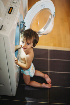 Young child in nappy climbing inside a washing machine