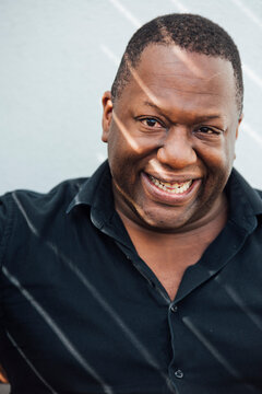A black man smiling at the camera with lines of sunlight on his face