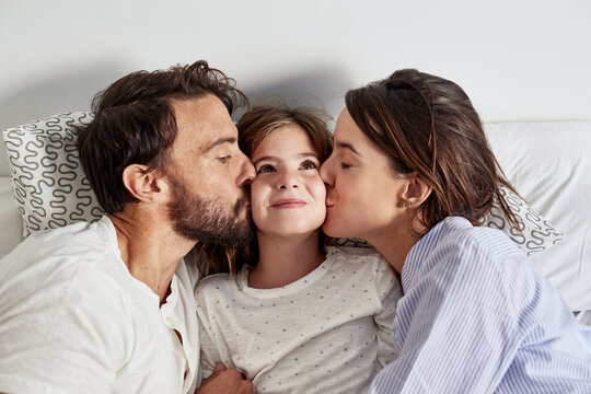 Loving Father And Mother Kissing Daughter In Bed