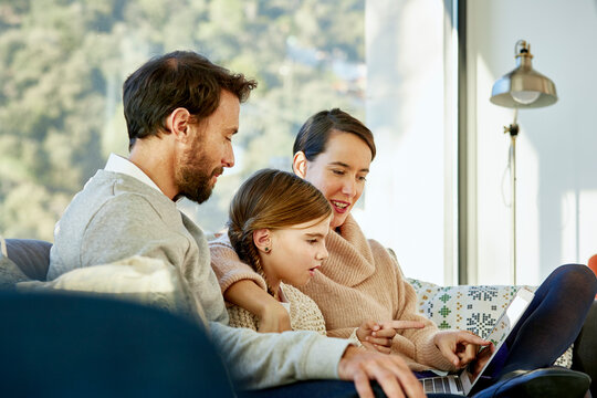 Girl With Mother And Father Using Laptop On Sofa
