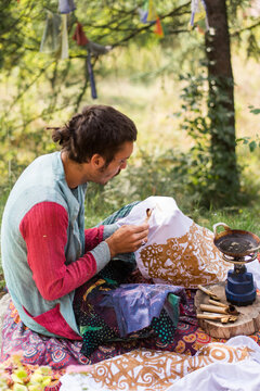 Young hippie man drawing some batik in nature