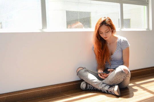 Mujer chateando por el celular sentada en el piso de su cuarto