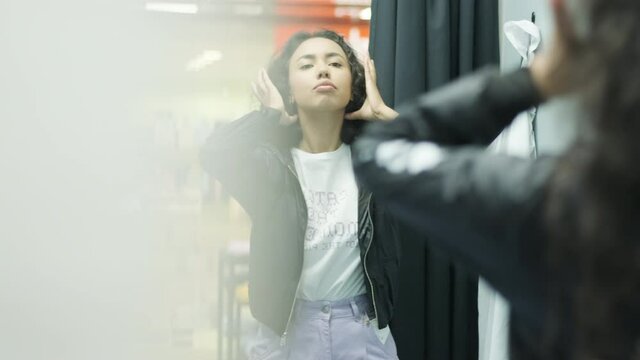 Happy, stylish girl trying on outfit in dressing room in interior boutique clothing store with bright lighting.