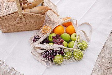 Picnic basket with baguette, bag with fruits on beach