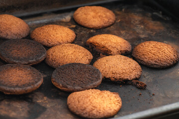 Burnt cookies. Burnt, burnt oatmeal cookies lie on a black baking sheet. Vertical photo