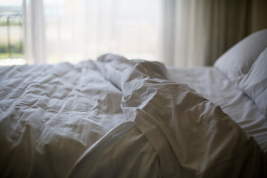 An Empty Bed Of Wrinkled White Sheets In The Morning