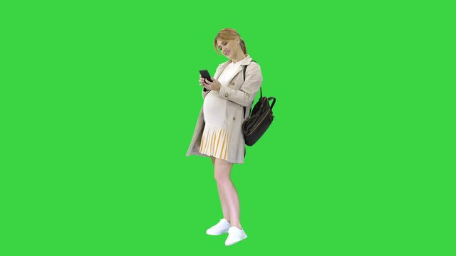 Pregnant casual woman holding cellphone texting a message on a Green Screen, Chroma Key.