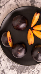 Plum whole and sliced on a black plate