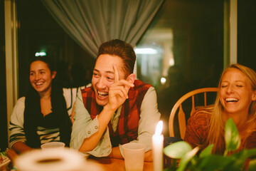 A group of friends sitting around a dining table laugh uncontrollably