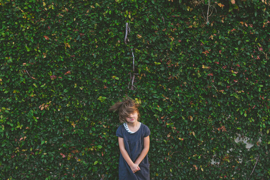 Young girl flips hair while standing in front of a vine-covered wall