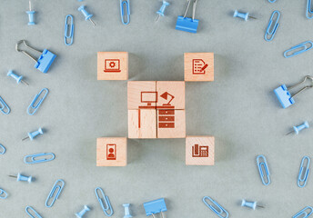 Conceptual of business office with wooden blocks with icons, paperclips, binder clips on sage color background top view. horizontal image