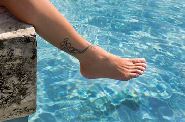 Piede sul bordo della piscina con tatuaggio sulla caviglia